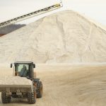 A wheel dozer carrying sand away from a large pile of sand