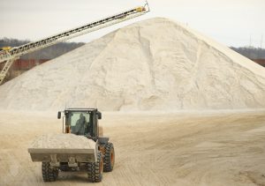 A wheel dozer carrying sand away from a large pile of sand